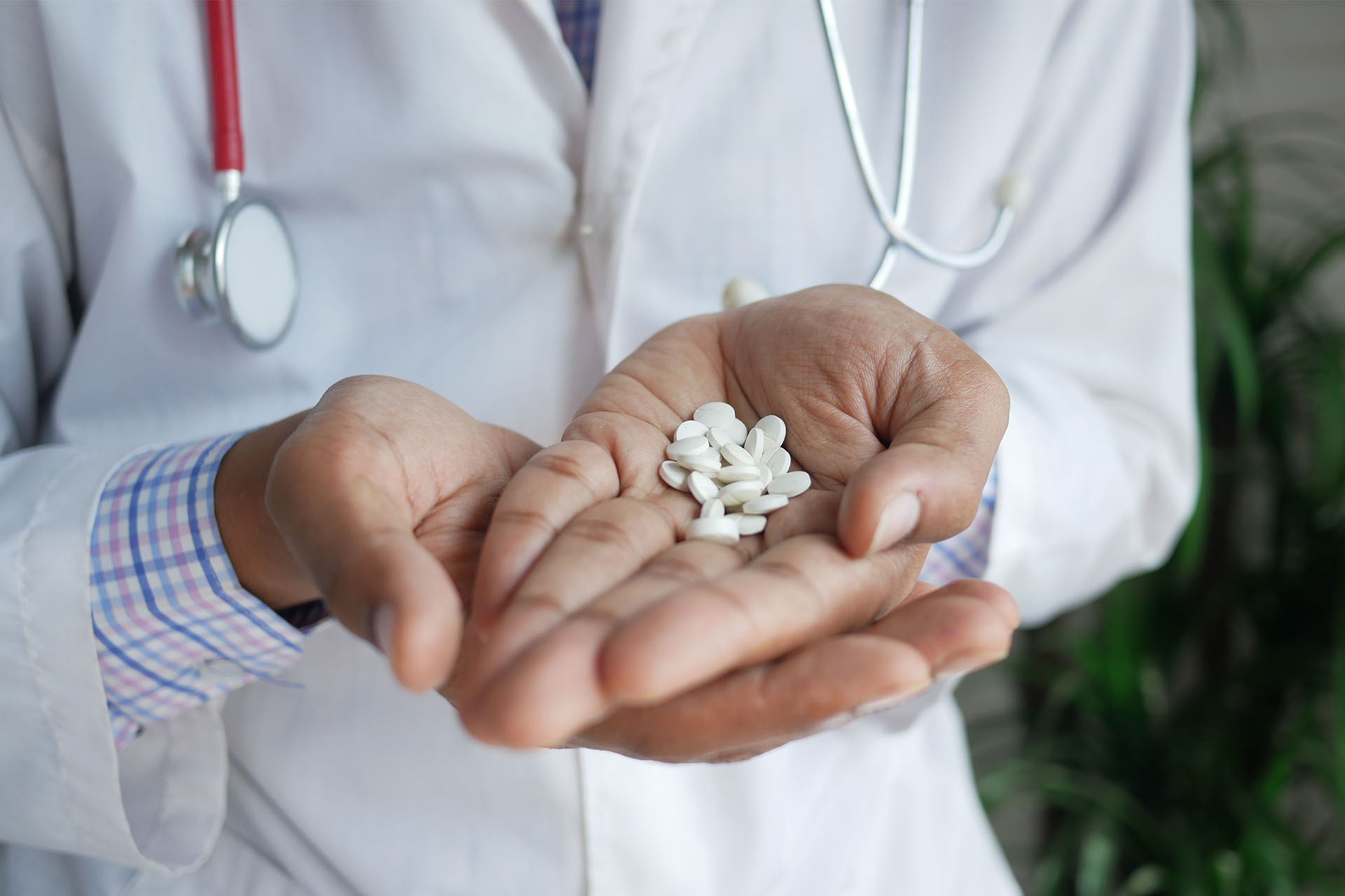 A medical professional in a white coat holds white pills in the palm of their hand