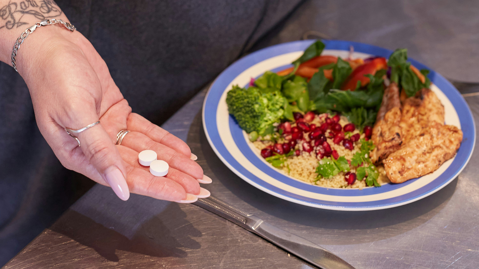 A person’s hand holding medication next to a plate of food